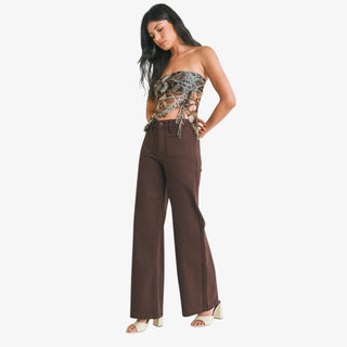 Woman wearing a strapless top with snake print and brown wide-leg pants on a white background