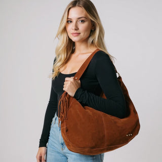 Woman holding a brown leather handbag against a plain background