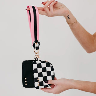 Black and white checkered pouch with pink and black strap held by a hand against a light background