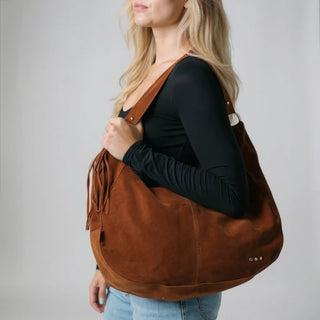 Woman carrying a brown leather handbag against a plain background