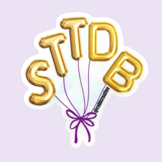 Gold balloon-shaped letters spelling 'STTDB' with a purple bow on a light purple background.