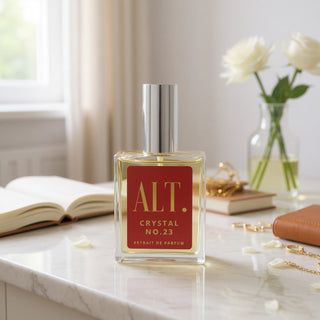 Perfume bottle labeled 'ALT. Crystal No.23' on a marble surface with books and flowers in the background.