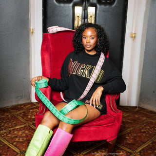 Model seated in red chair wearing Queen of Sparkles Licensed Black "Wicked" Logo Sweatshirt