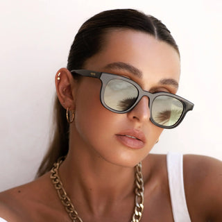 Woman wearing sunglasses and a gold chunky necklace and earrrings on a white background