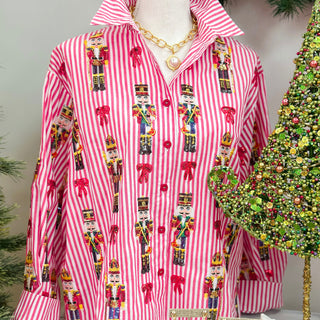 Red and White striped queen of sparkles button up shirt with multi color nutcrackers on it with a green christmas tree in the background.
