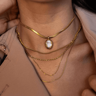 Layered gold chain necklaces with oval pearl pendant and snake chain detail styled with a neutral blazer for an elevated everyday look.