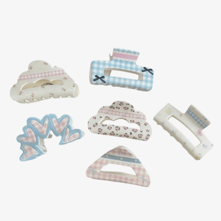 Set of pastel hair claw clips in assorted shapes with blue and pink gingham, floral, heart, bow, and leopard prints on a light grey background. 