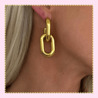 Close-up of a gold link drop earring featuring oversized oval chain links worn on a model’s ear against a soft pink background.