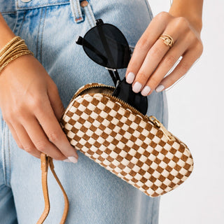 Handbag accessory woven checkered sunglasses case in tan and cream, shown with black sunglasses and gold zipper in lifestyle view.