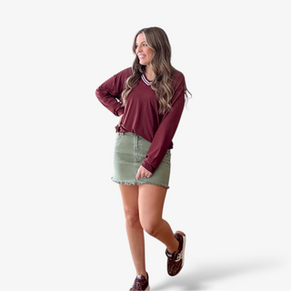 Woman wearing a maroon shirt, green skirt and leopard sneakers on a gray background