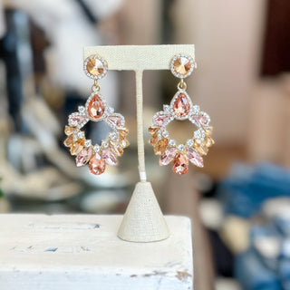 Blush and peach crystal chandelier statement earrings on gold-tone post backing displayed on stand.