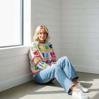 Lady sitting near a wall with a queen of sparkles abc sequined sweatshirt 