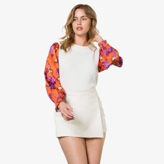Woman wearing an ivory sweater with long puff sleeves in orange and purple floral print.
