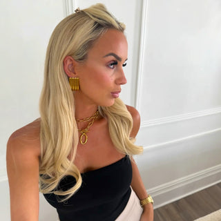 Woman wearing gold earrings and gold double layered necklace against a white wall