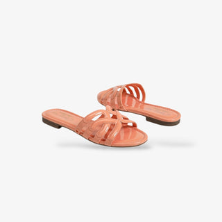 Coral patent leather slide sandals with open toe and cutout strap design, featuring a low heel and glossy finish for a chic, effortless summer look.