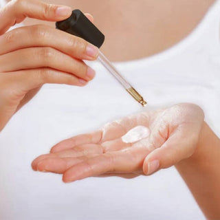 Hand applying a self tanning serum liquid from a dropper bottle onto another hand against a white background