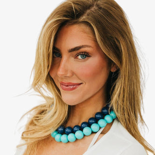 Turquoise bag charm necklace with oversized round beads and gold-tone clasps shown held outdoors in a front view.