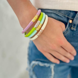 Blush pink, lime green, mint and ivory BuDhaGirl Three Kings Blossom II bangles stacked on wrist with gold crystal bead detail and denim outfit front view