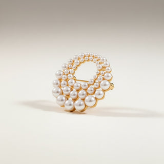 Pearl brooch pin with three circular rows of pearls and gold accents on a beige background