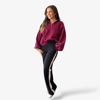 Lady wearing black and white stripe track pant with burgundy sweatshirt on a neutral background 