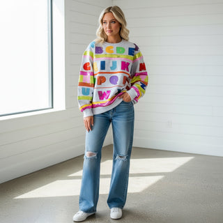 Woman wearing a Queen of sparkles abc sweatshirt with sequin letters and wide leg jeans 