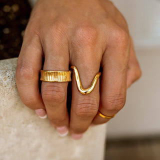 Hand wearing two gold rings on a neutral background