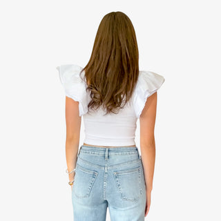 Person wearing a white top with ruffled sleeves and light blue jeans on a white background