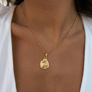 Gold necklace with a pendant on a person wearing a white top.