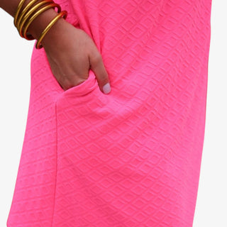 Close-up of a bright pink dress with a textured pattern, worn by a person with gold bangles.