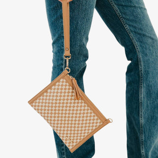 Tan woven crossbody clutch bag with cream checker pattern, wristlet strap, tassel and gold hardware shown carried at the hip in a front view.