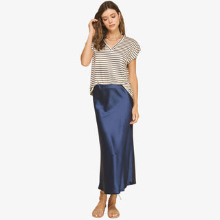 Women wearing a navy satin midi slip skirt styled with a striped V-neck t-shirt and sandals on a white background
