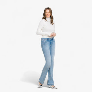 Woman wearing high rise light wash bootcut jeans with white long sleeve top and silver heels