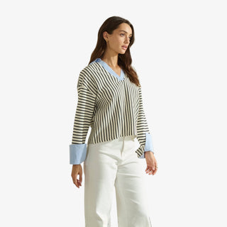 Woman wearing a black and white vertical striped blouse with light blue collar and cuffs, styled with white high-waisted pants.