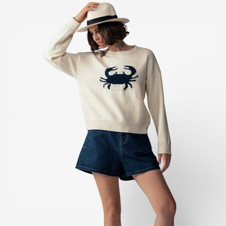 Woman wearing a cream sweater with a crab design and denim skirt on a white background