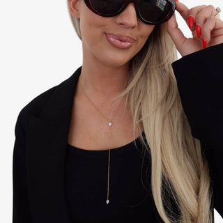 Gold lariat necklace with teardrop crystal detail worn with black top and blazer