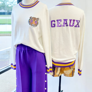 Mannequin wearing a cream sweater with a tiger logo and 'GEAUX' sequin text, purple pants.