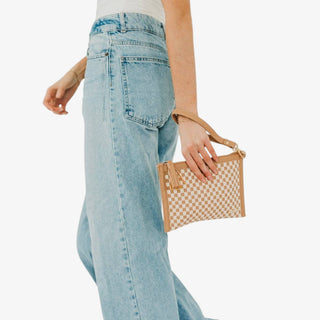 Tan woven crossbody clutch bag with cream checker pattern, wristlet strap, tassel and gold hardware shown carried at the hip in a front view.