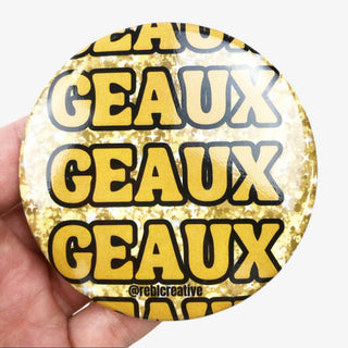 3-inch Geaux Geaux Geaux game day button with bold gold lettering outlined in black on a sparkling gold background, front view