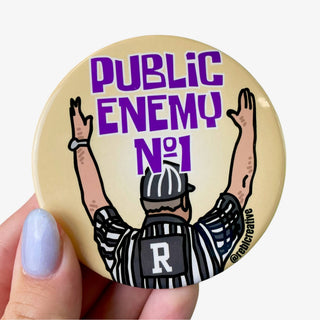 3-inch Public Enemy No. 1 game day button featuring a referee with raised arms and purple lettering on a gold background, front view
