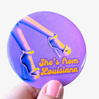 3-inch She’s from Louisiana game day button featuring high heels with gold lettering on a purple background, front view
