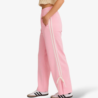 Pink bow track pants with white side stripes and ankle tie detail.