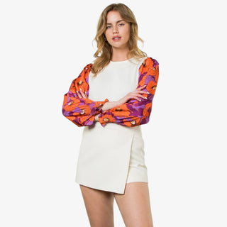 Woman wearing an ivory sweater with long puff sleeves in orange and purple floral print.