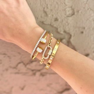 Close-up of a wrist wearing multiple gold and diamond bracelets against a neutral background