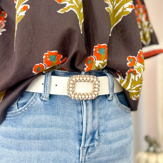 Ivory belt with a rectangular pearl and rhinestone buckle styled with denim jeans and a floral blouse, adding a chic touch to a casual outfit.