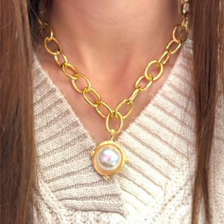 Gold chain necklace with a pearl pendant worn by a person in a light sweater.