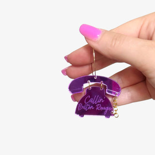 Purple Calling Baton Rouge hoop earrings featuring acrylic rotary phone charms with gold hoops displayed on a hand for size reference.
