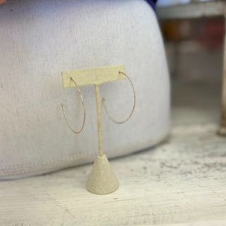 Dainty gold plated hoop earrings with thin textured design displayed on jewelry card with lace background