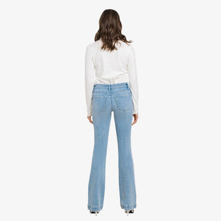 Woman wearing high rise light wash bootcut jeans with white long sleeve top and silver heels