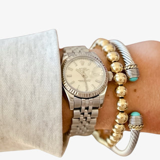 Silver watch and bracelets on a wrist against a white background