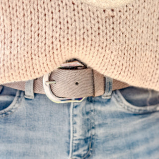 Woman wearing a platinum textured belt with a silver buckle and light denim jeans. 